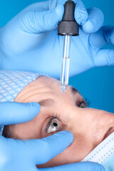 Optometrist throwing in liquid medication in to  a women's blue eyes