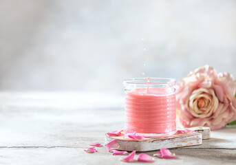 Ayurvedic rose moon milk with a little splash in the glass. A trendy relaxing form of drink before bed. Milk with rose petals on a light concrete background.