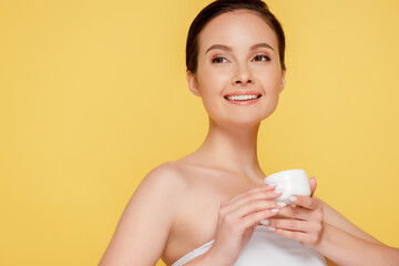 smiling beautiful woman holding container with cosmetic cream isolated on yellow