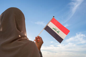 Silhouette of muslim woman in head scarf with Iraq flag at blue sunset sky. Concept of freedom