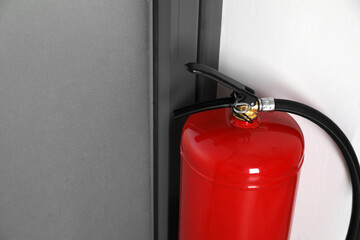 Obraz premium Fire extinguisher near door indoors, closeup. Space for text