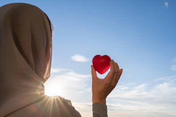 Silhouette of muslim woman in head scarf with red heart on blue sunset sky background. Concept