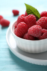 Delicious ripe raspberries in bowl on light blue wooden table, closeup