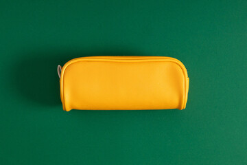 Bright yellow school pencil case, accessories on green background. Back to school. Flat lay, top...