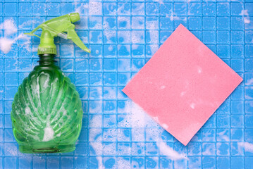 Cleaning tool sprayer and pink rag with white foam on a blue wall with cages