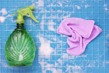 Cleaning tool sprayer and pink wrinkled cloth with white foam on a blue wall with cages