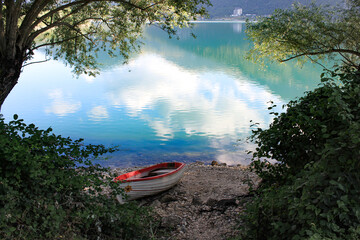 white boat on the shore of Lake Scanno, Abruzzo. Colorful reflections on the water in a summer landscape surrounded by nature. Frame of green vegetation. Glimpse of calm, tranquility and relaxation. 