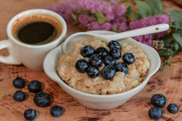 Oatmeal with blueberries for breakfast with coffee on a wooden table. Traditional healthy breakfast. Oatmeal and espresso. Close-up