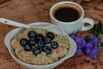 Oatmeal with blueberries for breakfast with coffee on a wooden table. Traditional healthy breakfast. Oatmeal and espresso. Close-up
