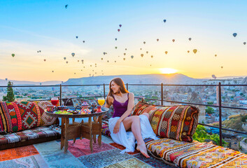 A woman have breakfast on one of the Cappadocia roof in early morning sunrise, when balloons fly. Romantic scene Cappadocia, Turkey.