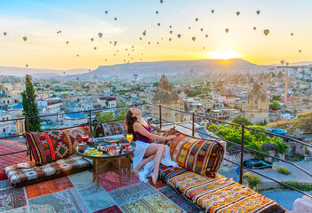 A woman have breakfast on one of the Cappadocia roof in early morning sunrise, when balloons fly. Romantic scene Cappadocia, Turkey..