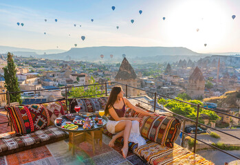 A woman have breakfast on one of the Cappadocia roof in early morning sunrise, when balloons fly. Romantic scene Cappadocia, Turkey.