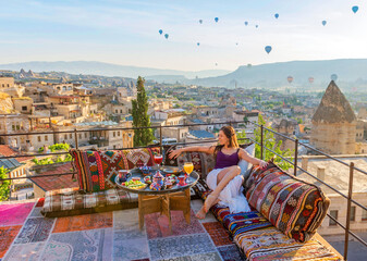 A woman have breakfast on one of the Cappadocia roof in early morning sunrise, when balloons fly. Romantic scene Cappadocia, Turkey.