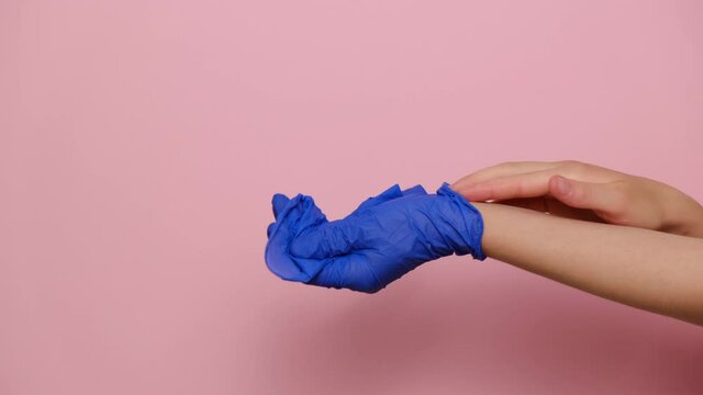 Close up of unrecognizable young woman removes blue medical gloves and throw it in trash, isolated on pink studio background with copy space for advertisement. Concept end of virus epidemic