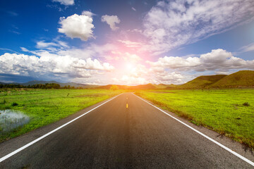 Open road through the green field and clouds on blue sky in summer day. Highland road.