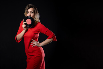 Obraz premium blonde girl in a red dress with vinyl records in hands on a black background with copy space