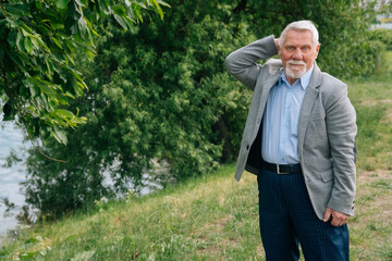A brooding stylish old man in a business suit against the background of the forest.