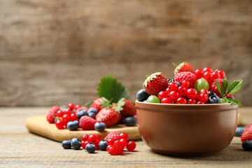 Mix of different fresh berries in bowl on wooden table. Space for text