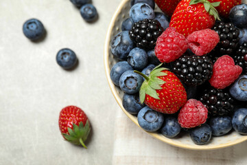Mix of different fresh berries in bowl on light grey table, flat lay. Space for text