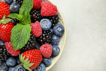 Mix of different fresh berries and mint in bowl on light grey table, top view. Space for text