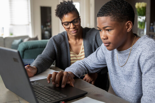 Mother Helping Teen Son With Homework At Dining Table