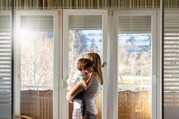Shot of loving mother carrying her boy at home.Rear view portrait of family on balcony looking through the window.Shot of single mother and her adorable little son looking out the window at home.