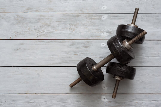 Old black dumbbells on a wooden floor background. Simple gym flat lay background with copy space.