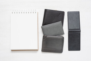 Blank page notepad with empty pages for copy space and various leather wallets on white flat lay background.