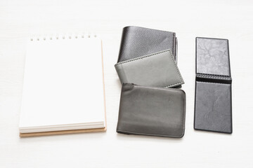 Blank page notepad with empty pages for copy space and various leather wallets on white flat lay background.