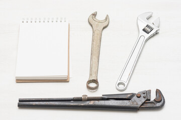 Fix list template. Notepad with blank page and wrenches on the white wooden table background.