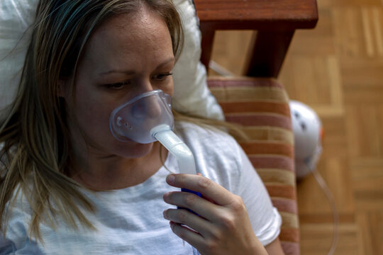 Woman's Face Inhaling Through Inhaler Mask.Female Patient Inhalation Therapy With Mask Of Inhaler With Soft Stream Smoke From Asthma Inhaler.Self-treatment Of The Respiratory Tract Using Inhalation.