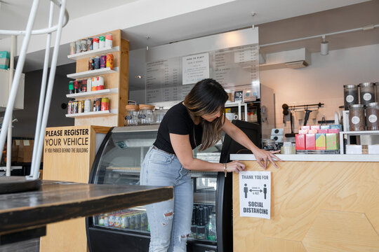 Young woman putting safety distance poster on cafe counter