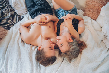 Young loving couple caress each other. They care and kiss and hug each other with love. Summer portrait at home on the bed in casual outfit