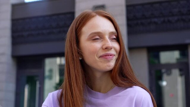 Close-up of face of smiling redhead girl looking around, background of modern city street. Portrait of beauty young woman feeling happy outdoors. Cheerful lady standing on urban outside. closeup.