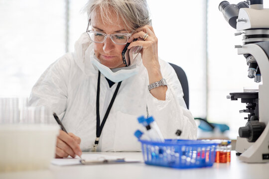 Medical researcher using phone and writing notes in laboratory