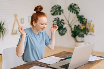 Cheerful redhead young businesswoman is working laptop and getting good message at remote work...