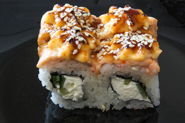 Japanese sushi food on the black plate. Baked warm rolls with tuna, salmon, shrimp, crab and avocado. Top view of assorted sushi.