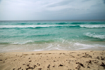 Vacations. Seascape. Turquoise color water sea. The white sand and ocean waves under a dramatic stormy sky in Cancun, Mexico.