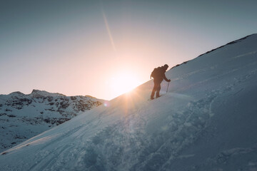 Naklejka na ściany i meble Man mountaineer with trekking pole climbing on snowy hill and sunshine at Ryten mount