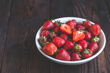 Fresh strawberries in a white bowl on wooden table with low key scene. copy space