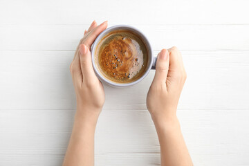 Woman with cup of coffee at white wooden table, top view