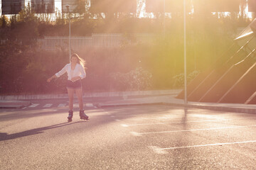 Blonde girl in white blouse and jeans skating in the city at sunset. Roller-skating concept