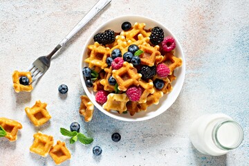 Tiny (Mini) waffles waffles with milk for breakfast with berries in a white bowl on a light background.