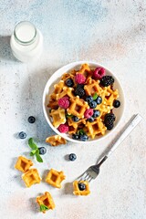 Tiny (Mini) waffles waffles with milk for breakfast with berries in a white bowl on a light background.
