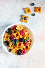Tiny (Mini) waffles waffles with berries in a white bowl on a light background.