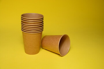 Brown paper cups close up on  paper cups, scattered, bow, brown . Recycling craft paper cup of coffee to go on neutral background. Selective focus. Craft cup for hot beverage, takeaway. Disposable cup