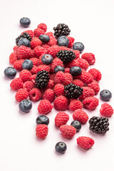 Ripe raspberries with blackberries and blueberries on light backgournd.