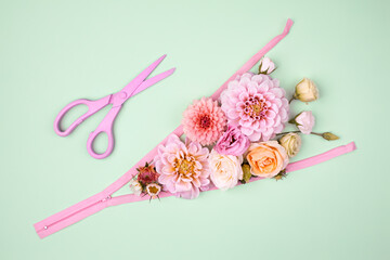 Close Up of flowers amidst zipper by scissors on pastel blue background
