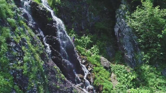 Beautiful waterfall in the mountains on a summer sunny day and a girl nearby, filmed by drone