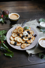 Mini pancakes in a light plate on a wooden table. Breakfast with coffee, pancake cereal and berries.